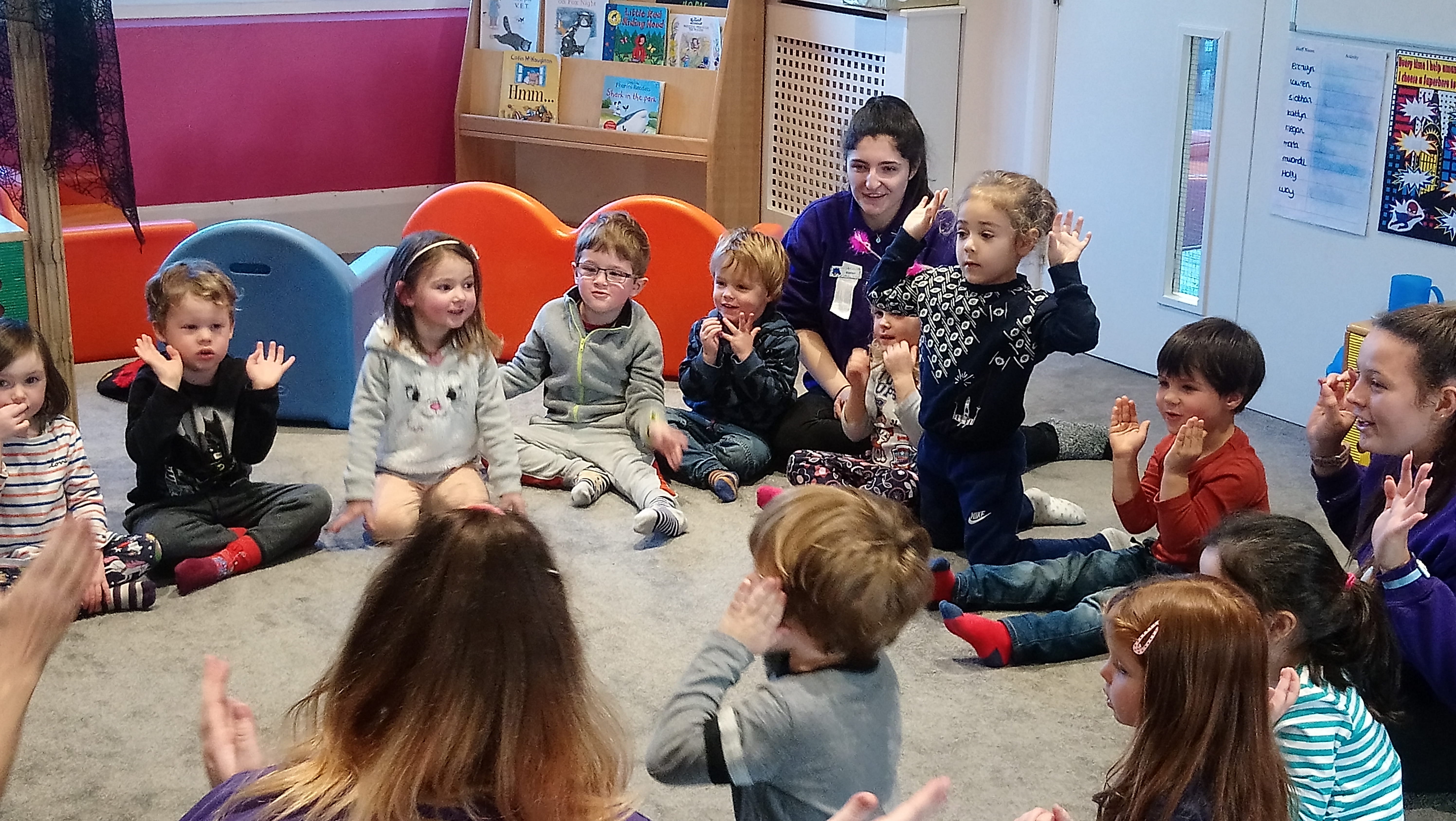 Group of young children sitting in a circle with their hands in the air