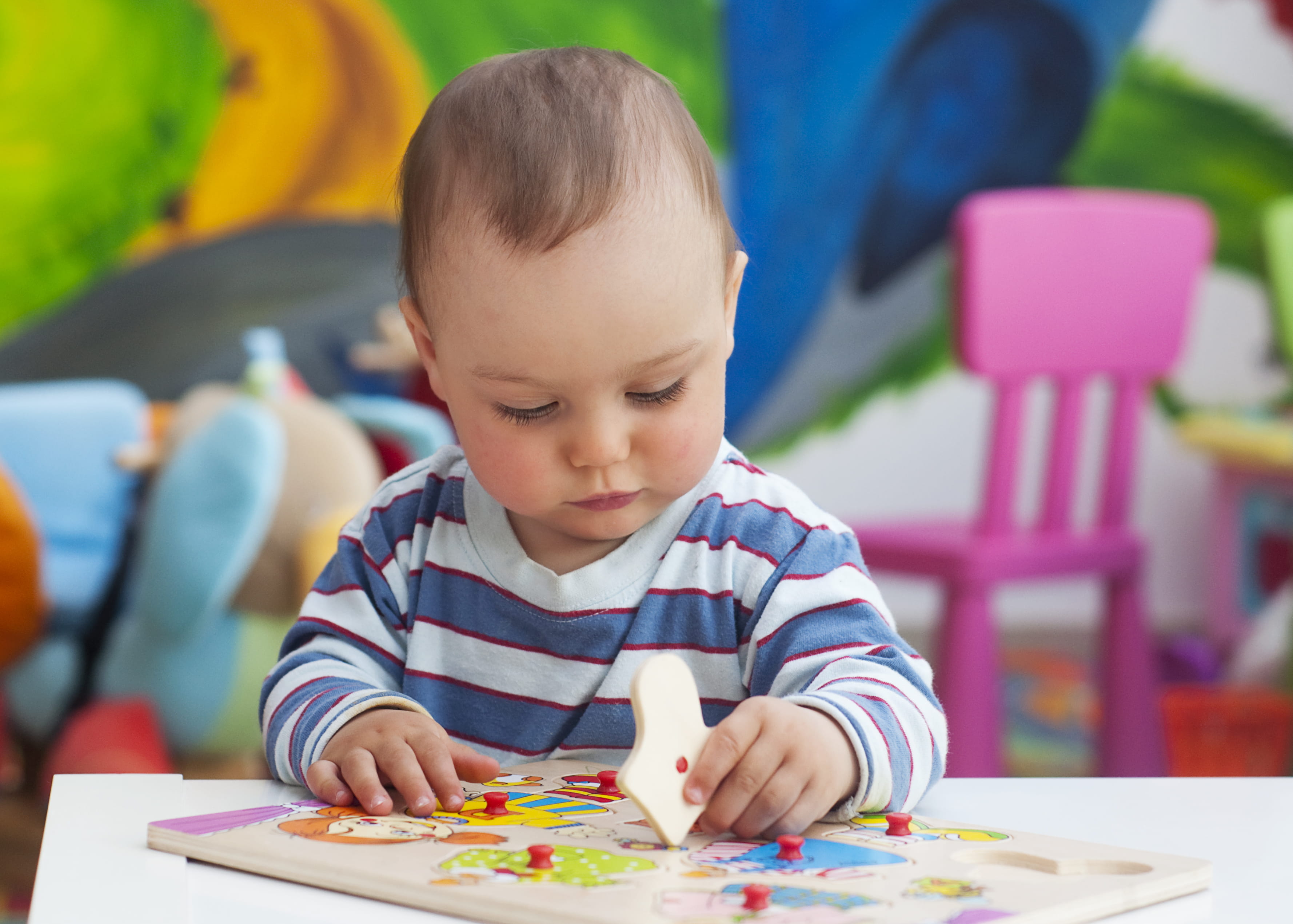 Small toddler playing with puzzle shapes on a low table in a colorful nursery room