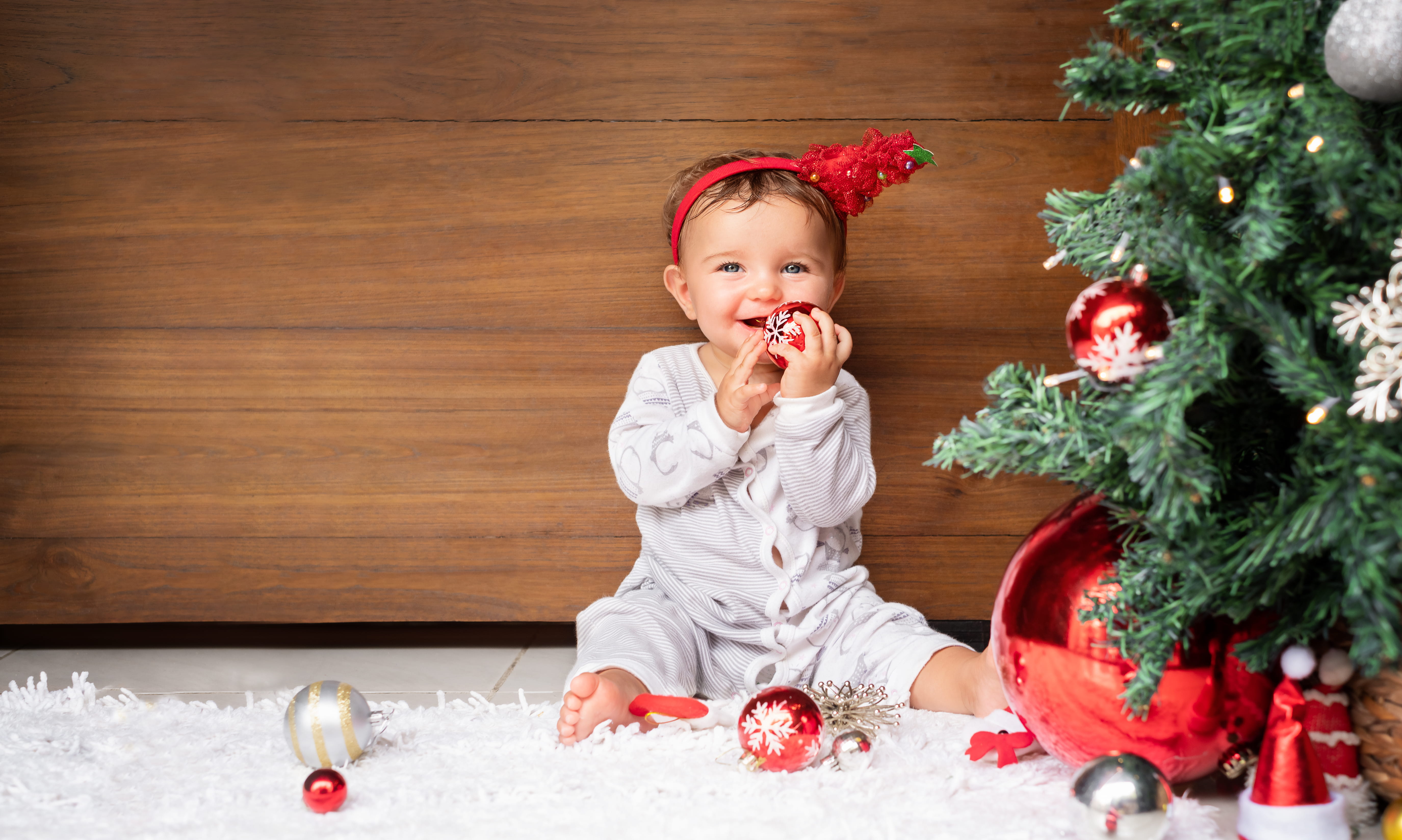 Portrait of baby on the wooden background holding ornament near the Christmas tree.