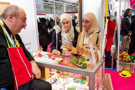 Two ladies standing at children's craft stand with gentleman sitting behind stand at the Childcare and Education Expo 