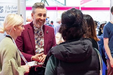 International Early Years consultant, Alistair Bryce-Clegg, smiling and talking with a group of exhibitors at the Childcare and Education Expo 