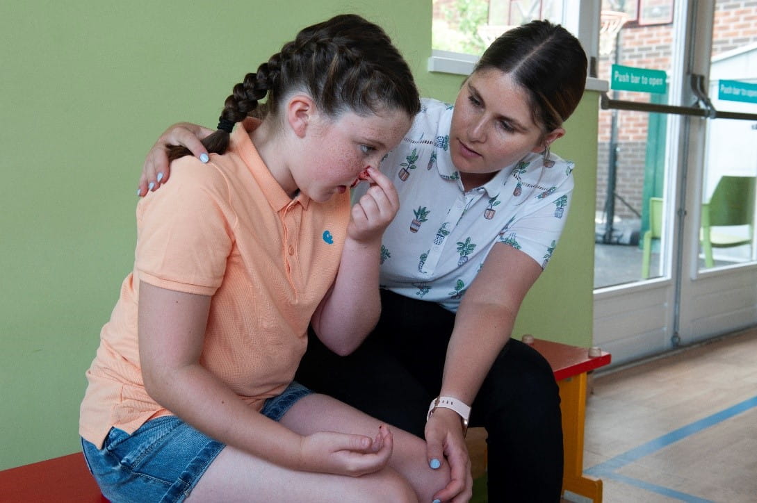 Woman comforting child who is pinching their nose to help stop nose bleed