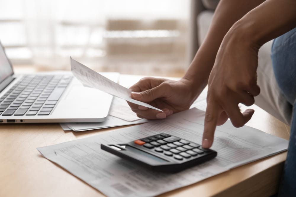 Close up of woman holding paper bills using calculator and laptop