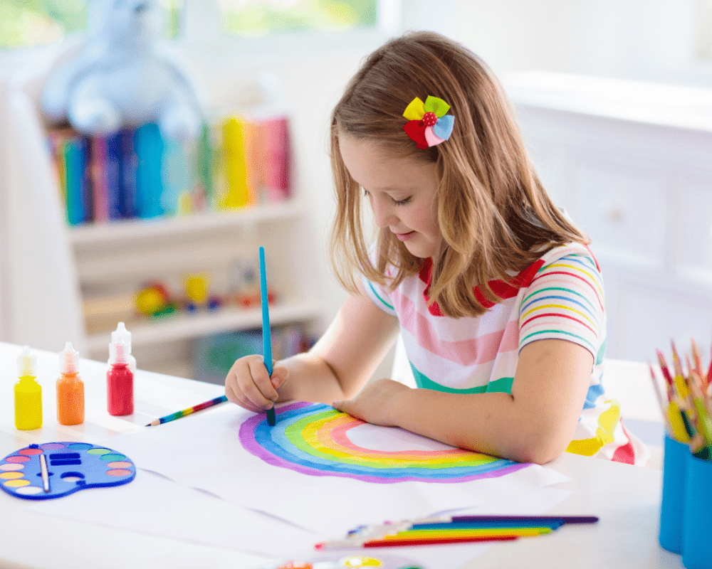 Young girl child sitting at table painting a rainbow