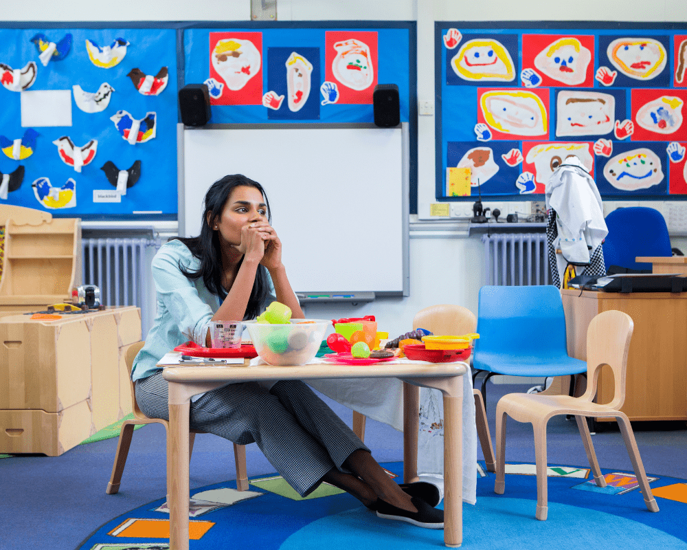 Stressed nursery teacher sitting in a classroom at children's toy table