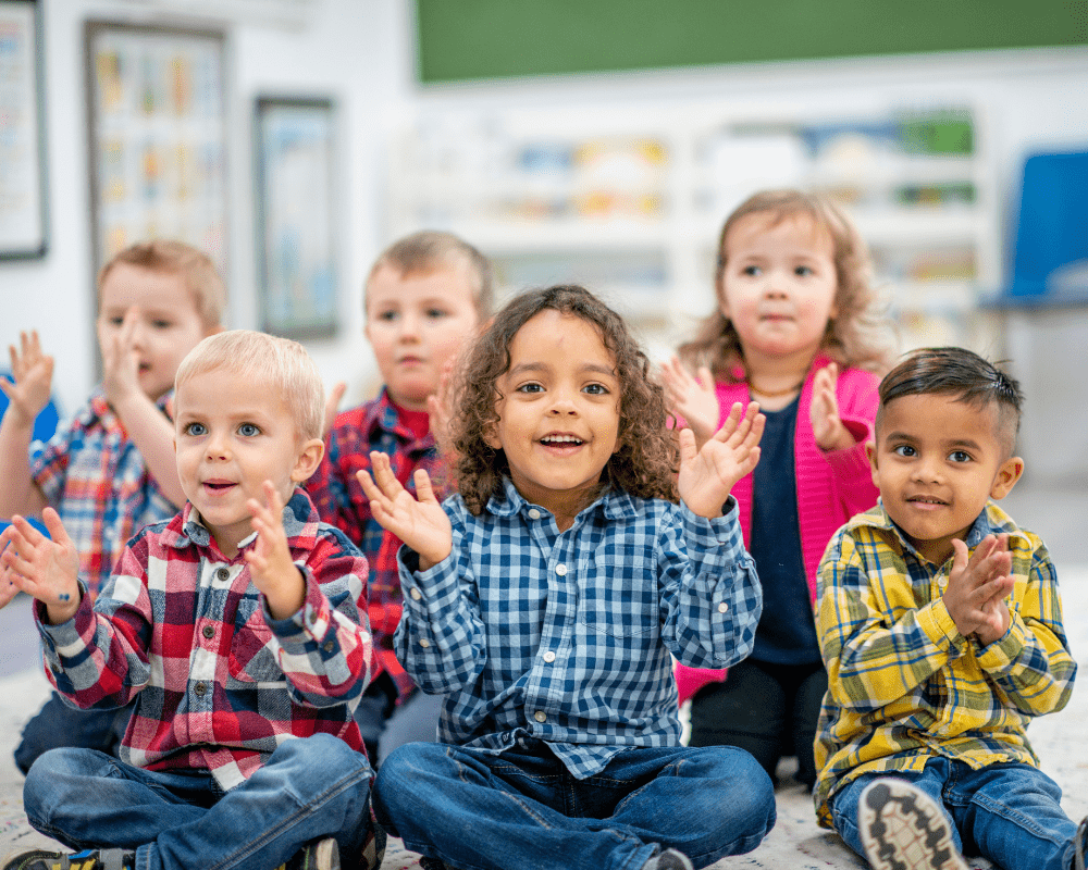 Happy group of preschool aged children sitting on mat in a classroom setting