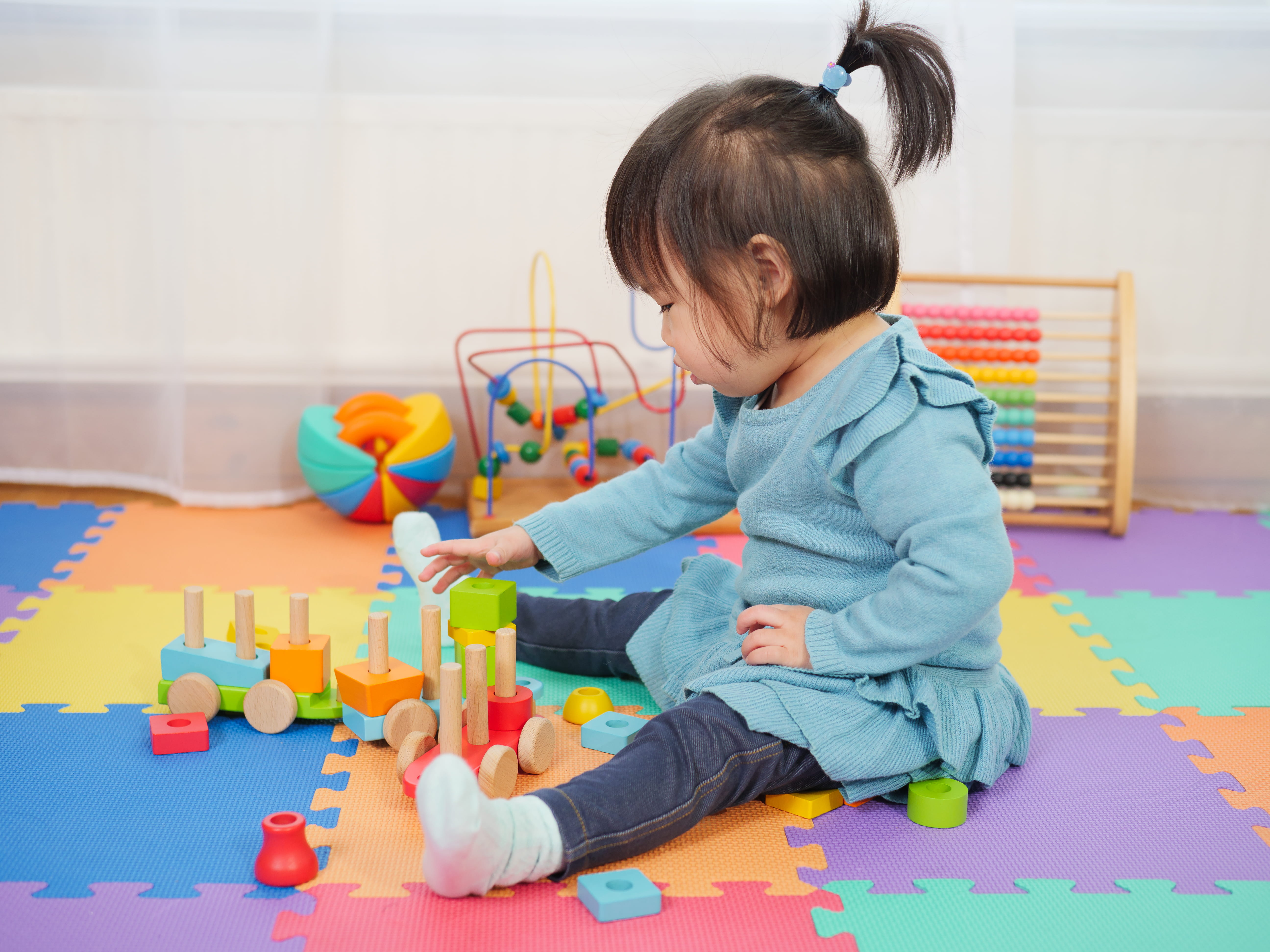 Toddler playing with colourful wooden toys on colourful foam puzzle play mat