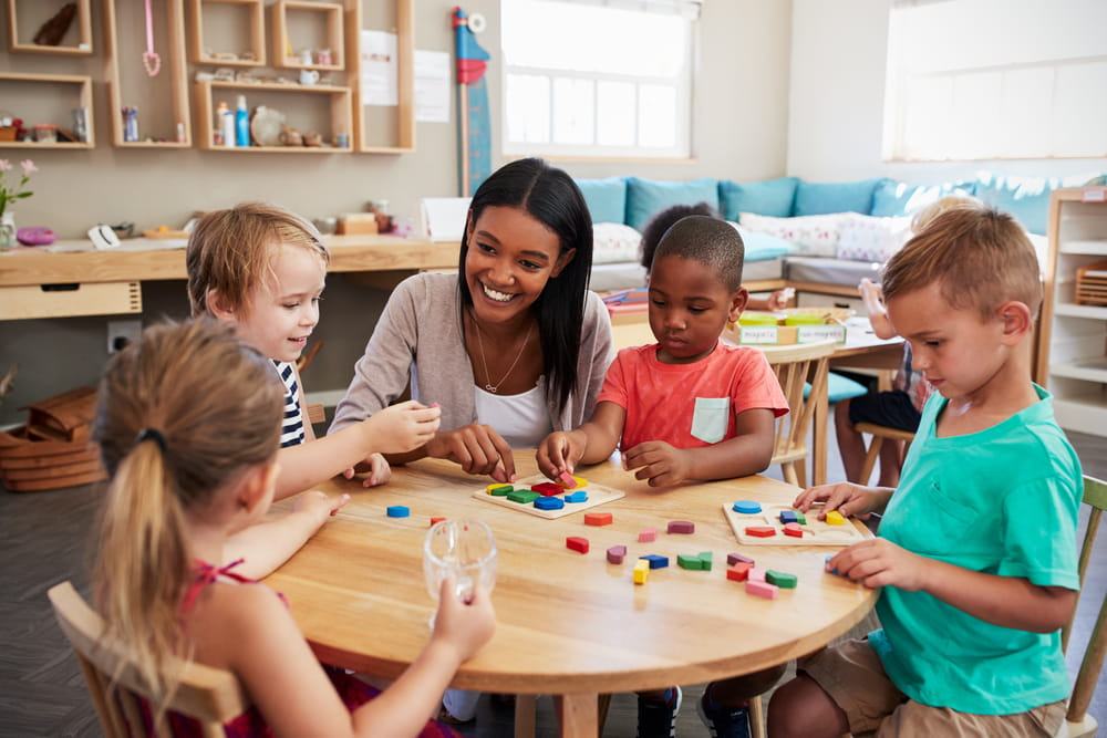 Smiley teacher and preschool children sitting at table learning and playing together