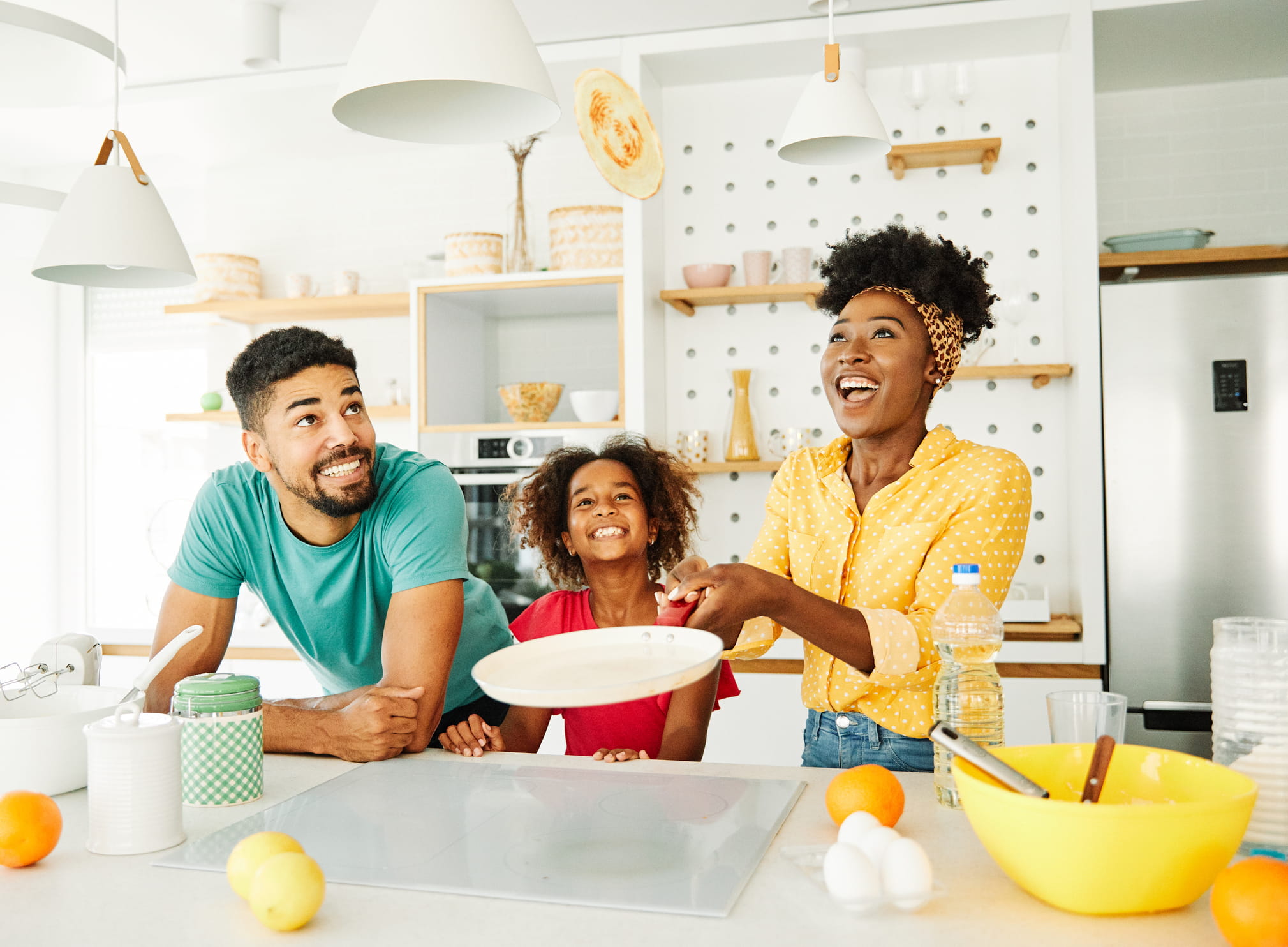 Smiley family making pancakes together in kitchen, lady holding the frying pan and flipping pancake