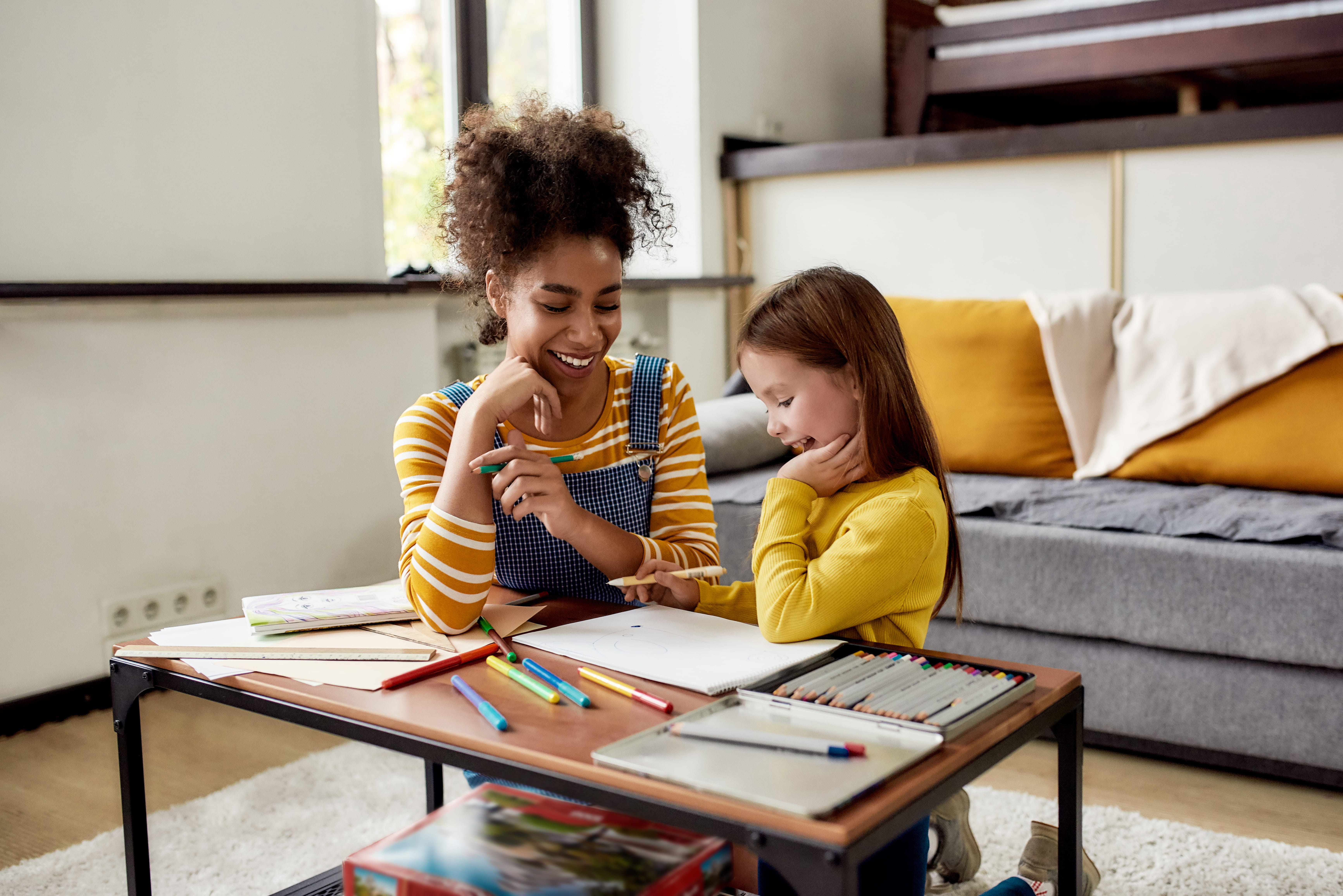 Little girl spending time with childminder. They are drawing, learning how to draw, sitting on the floor.