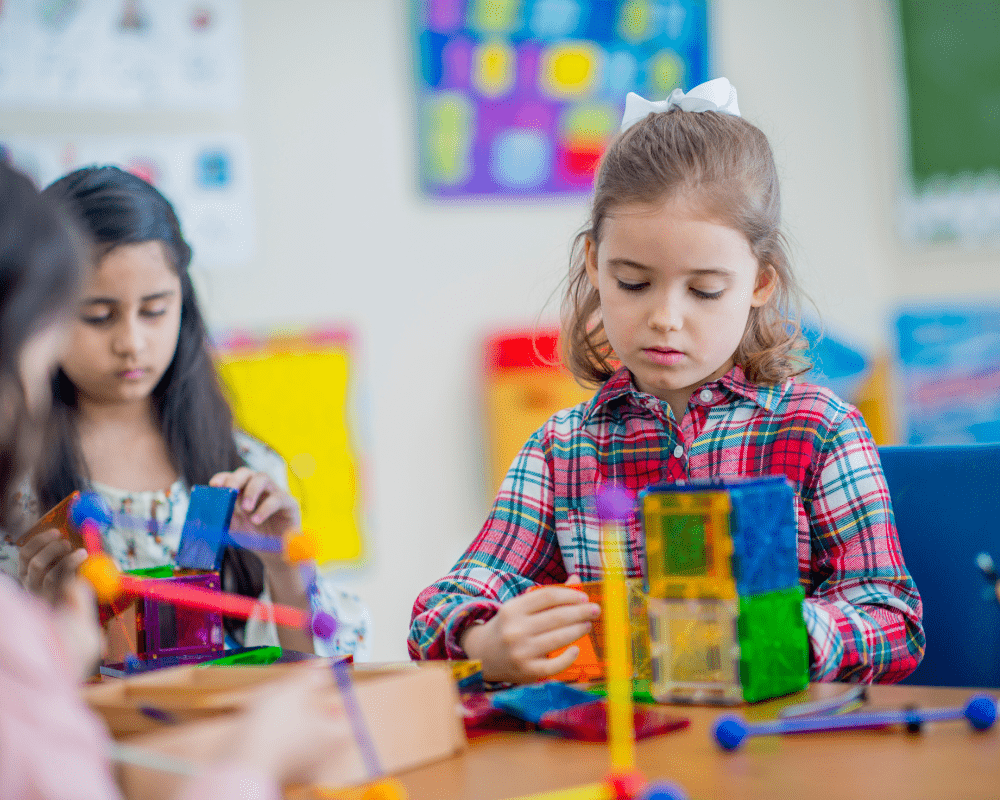 Group of young school kids in wraparound care club sitting at a table playing and building shapes