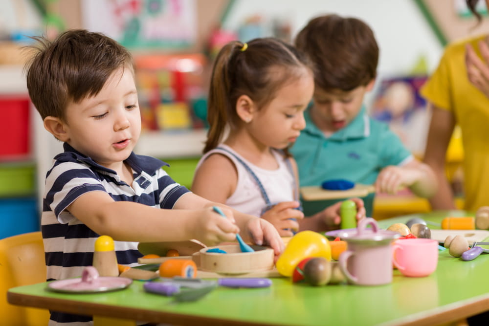 Young children playing with crockery toys while sitting at a table together in classroom 