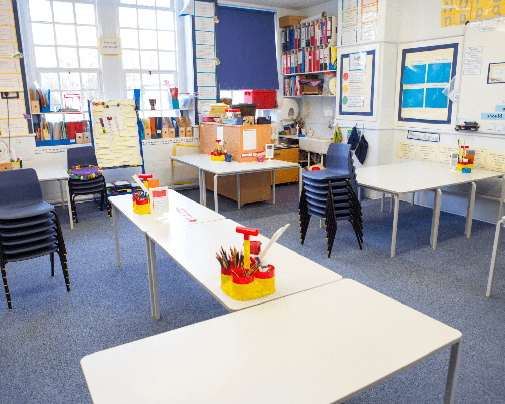 A horizontal image of an empty primary school classroom. The setting is typically British