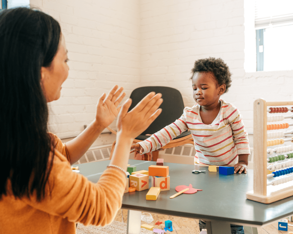 Nursery school teacher playing with young child, with colourful block toys