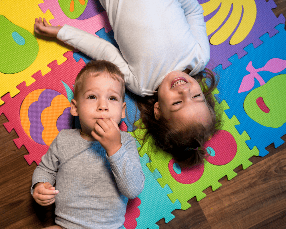 Two happy toddlers lying down and playing on colourful foam puzzle mat