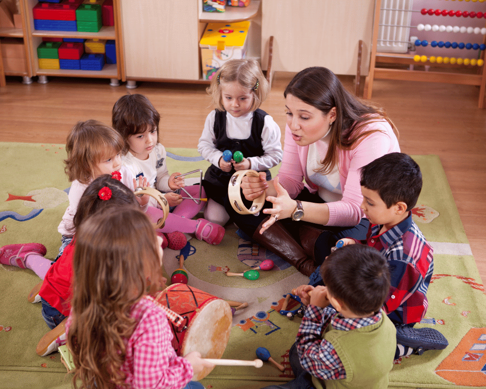 A group of preschool or nursery school children in classroom with teacher sitting on the floor together and playing musical instruments