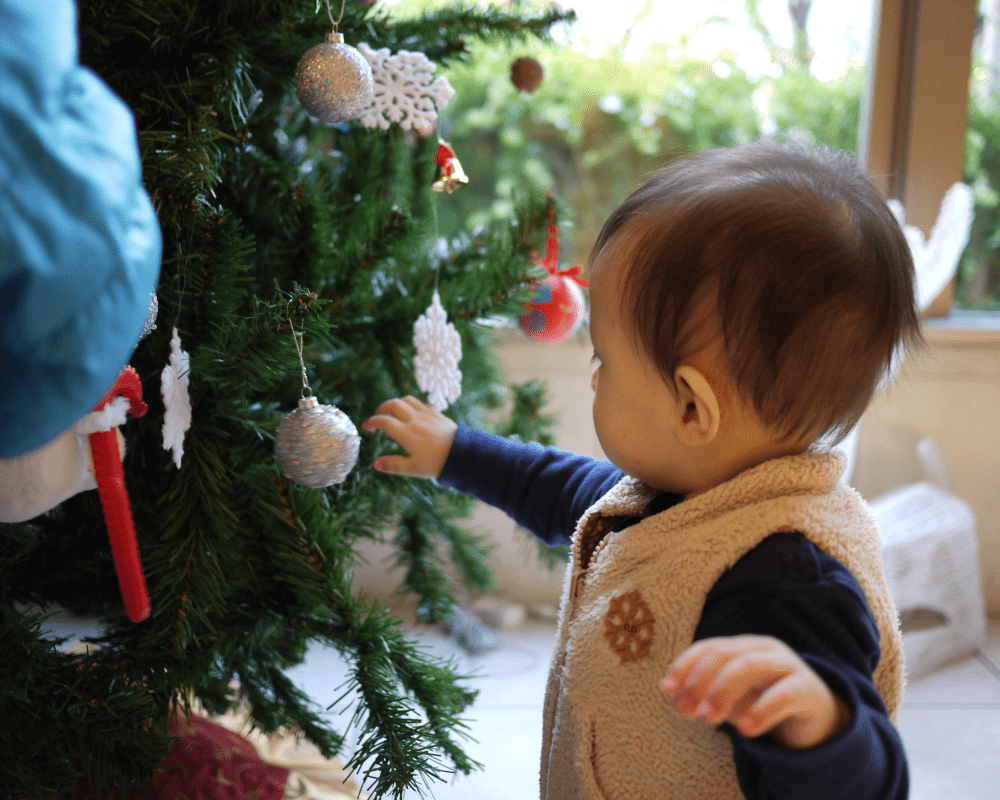 Toddler touching a bauble on a Christmas tree at home
