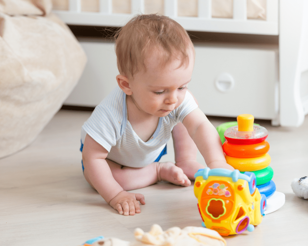9 months old baby playing with colourful toys on the floor in bedroom