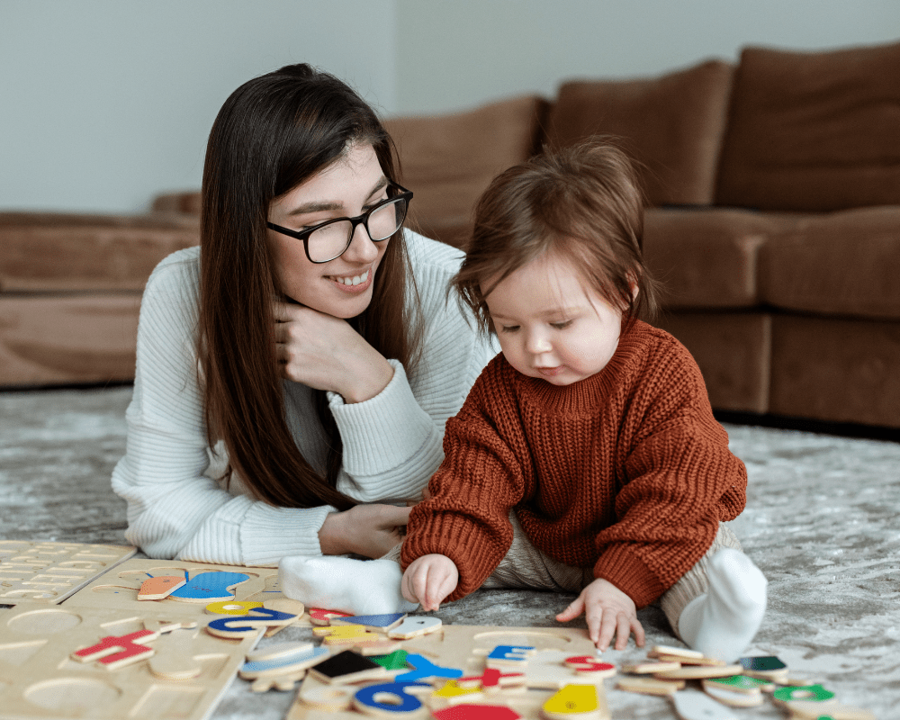 Childminder and toddler playing with wooden educational letters and numbers games on a rug in a living room