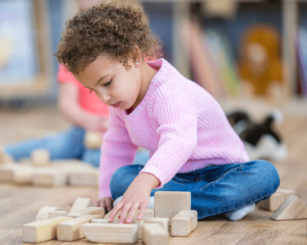 Child playing with wooden blocks on the floor in preschool classroom