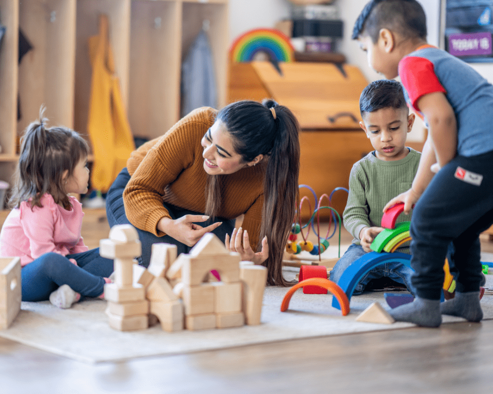 Kindergarten teacher sitting on floor with students as they play