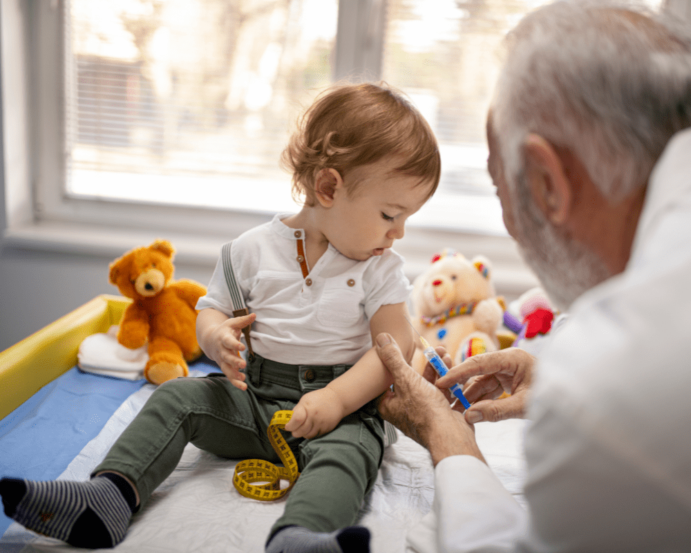Toddler getting vaccinated in doctor's office with teddies sitting around him
