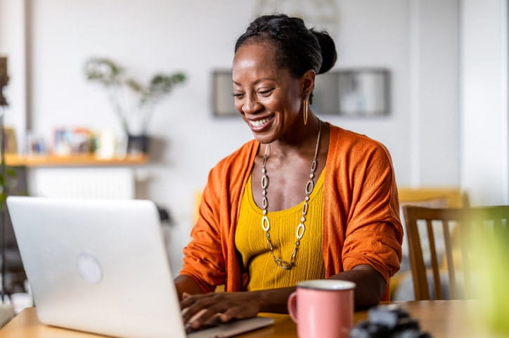 Smiling woman in orange cardigan browses her laptop at home
