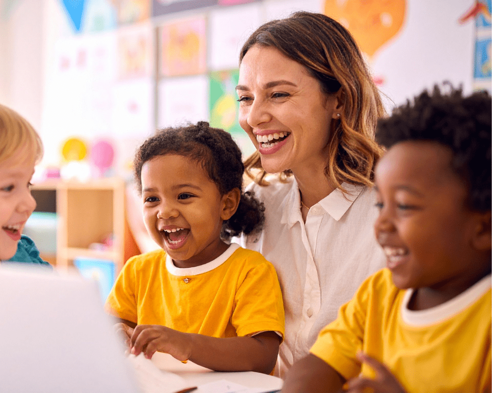Teacher and preschool students sitting together in classroom smiling.