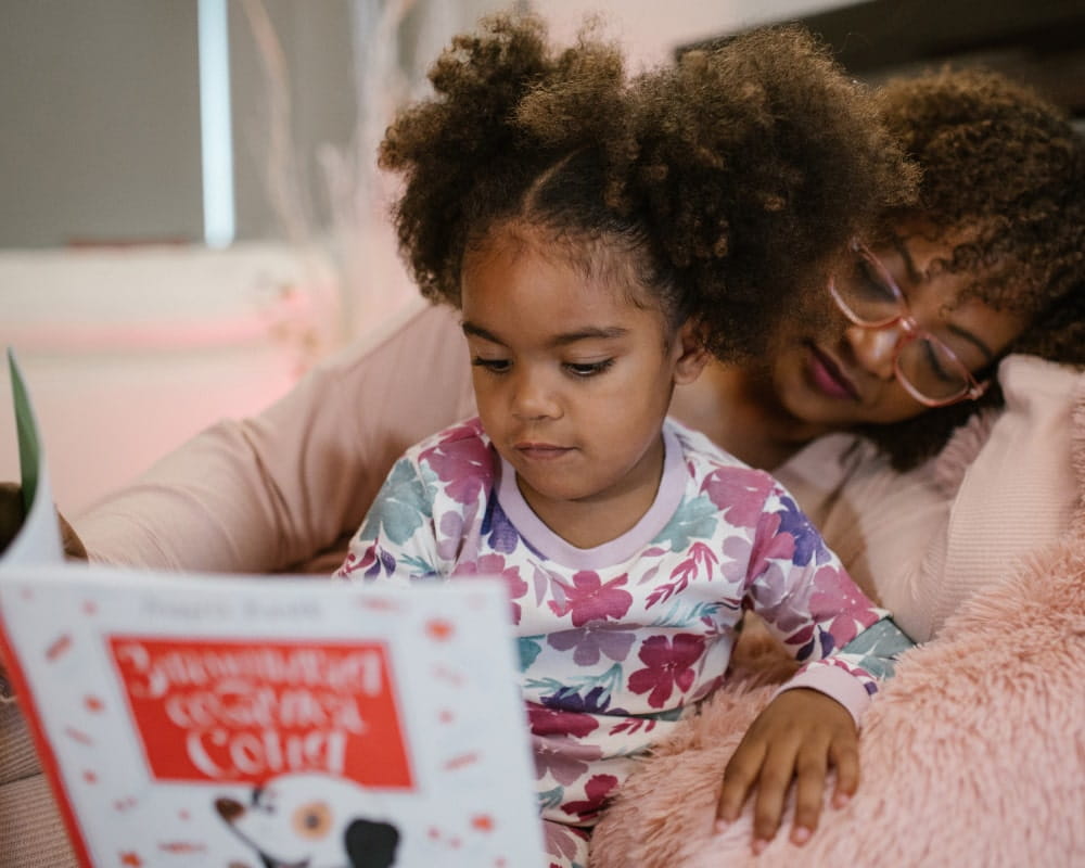 Young girl is reading a bedtime story next to her mother on her bed