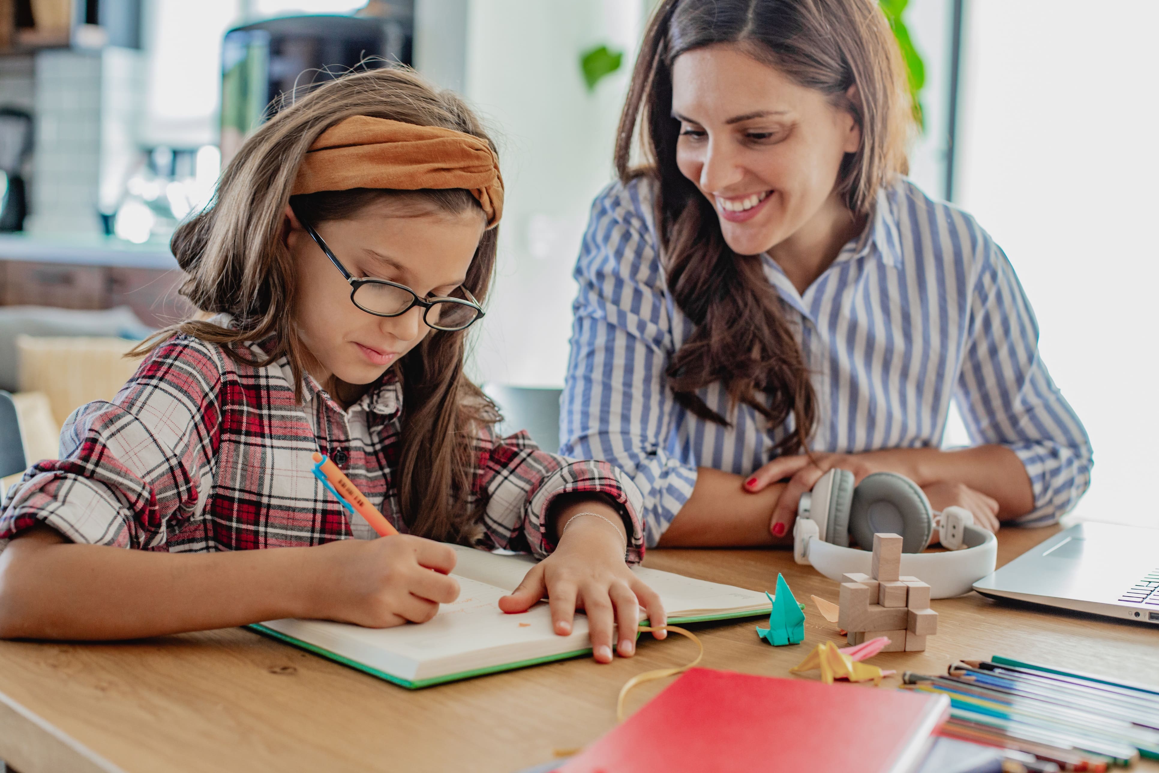 A female tutor smiles as she helps a young girl write in her book