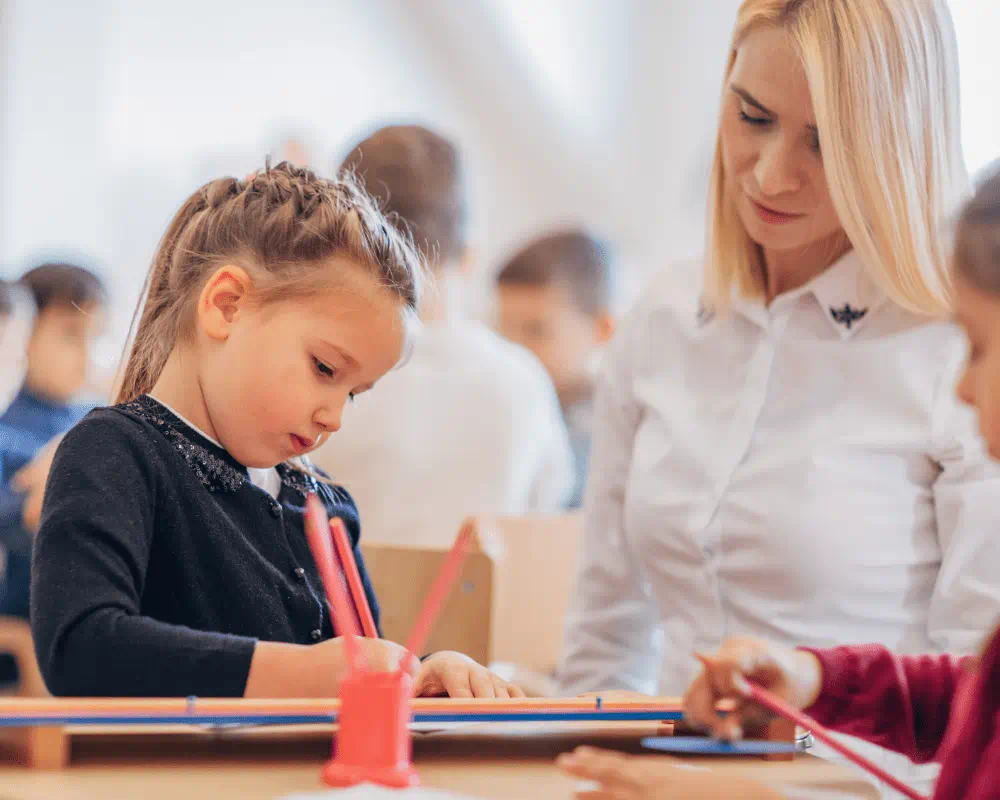 Teacher helping two young girls with learning in classroom 