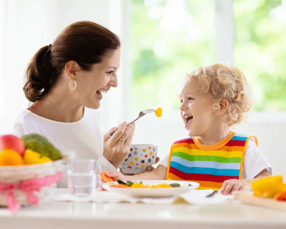 Mother feeding child vegetables. They are both smiling at each other.