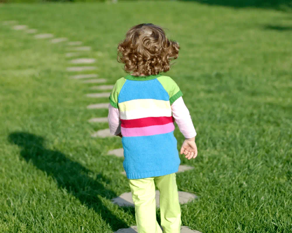Child facing away from camera walking outdoors on stepping stones laid out on grass