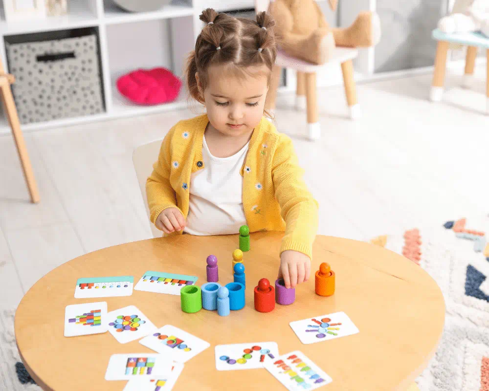 Little girl playing with colourful toys at wooden table indoors 