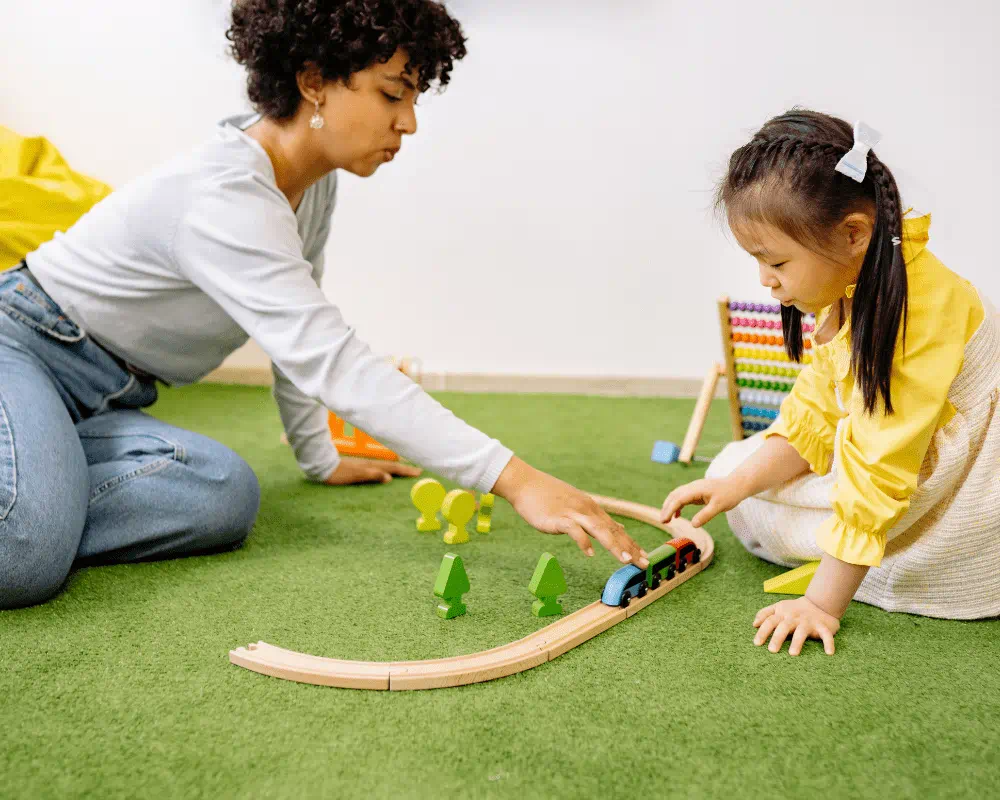Woman playing wooden toy train with a little girl 