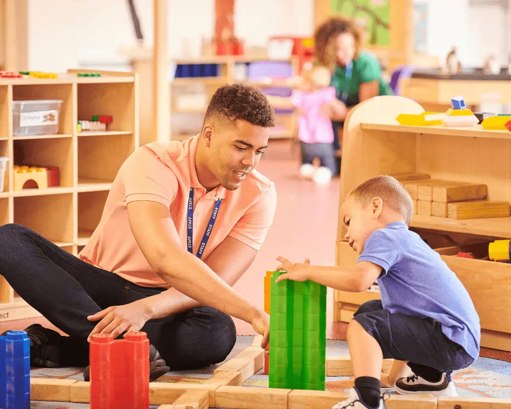 Male nursery school teacher playing colourful blocks with little boy