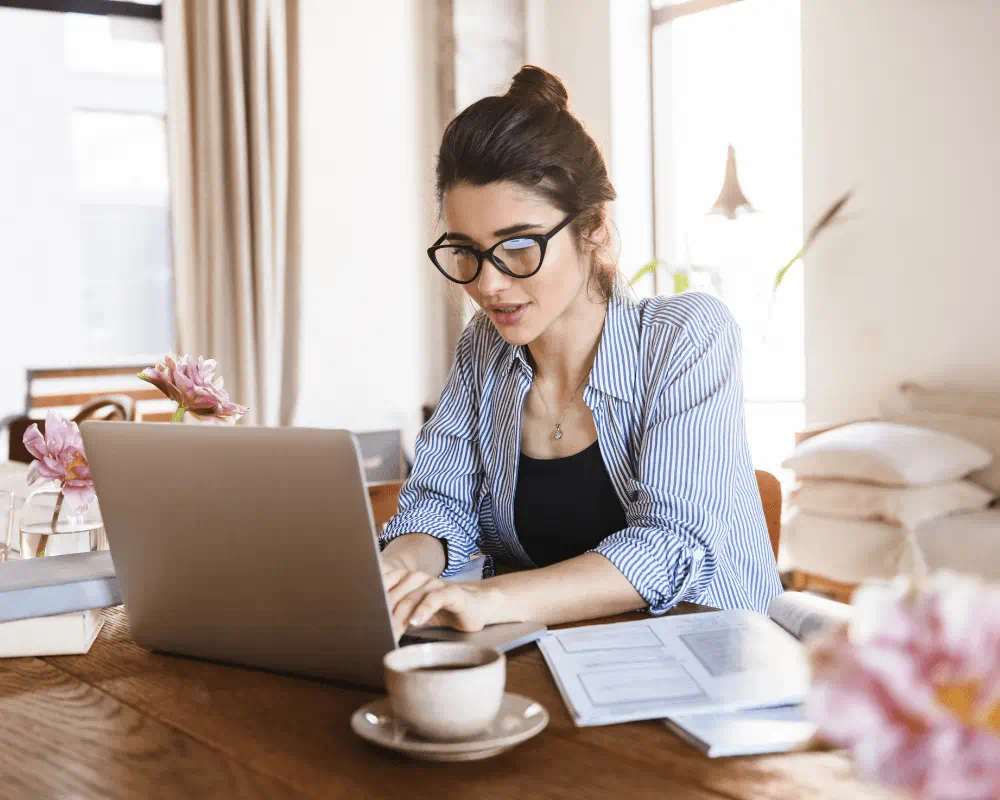 Woman casually dressed with glasses typing on laptop while working or studying from home 