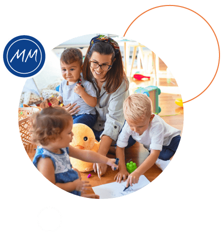 A childcarer playing with 3 young children in a nursery setting.