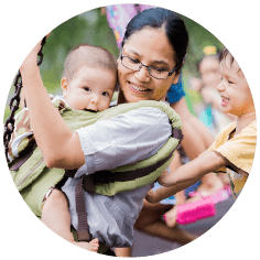 A  photograph of a carer holding a small baby in a playground.