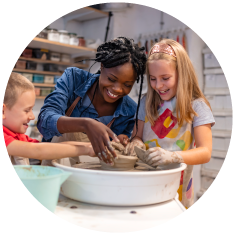Two children and a lady smiling whilst doing pottery together