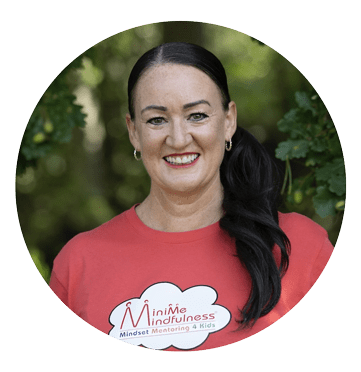 Headshot of a smiling woman with dark hair and wearing a red jumper with white motif, standing against a backdrop of green leaves and trees