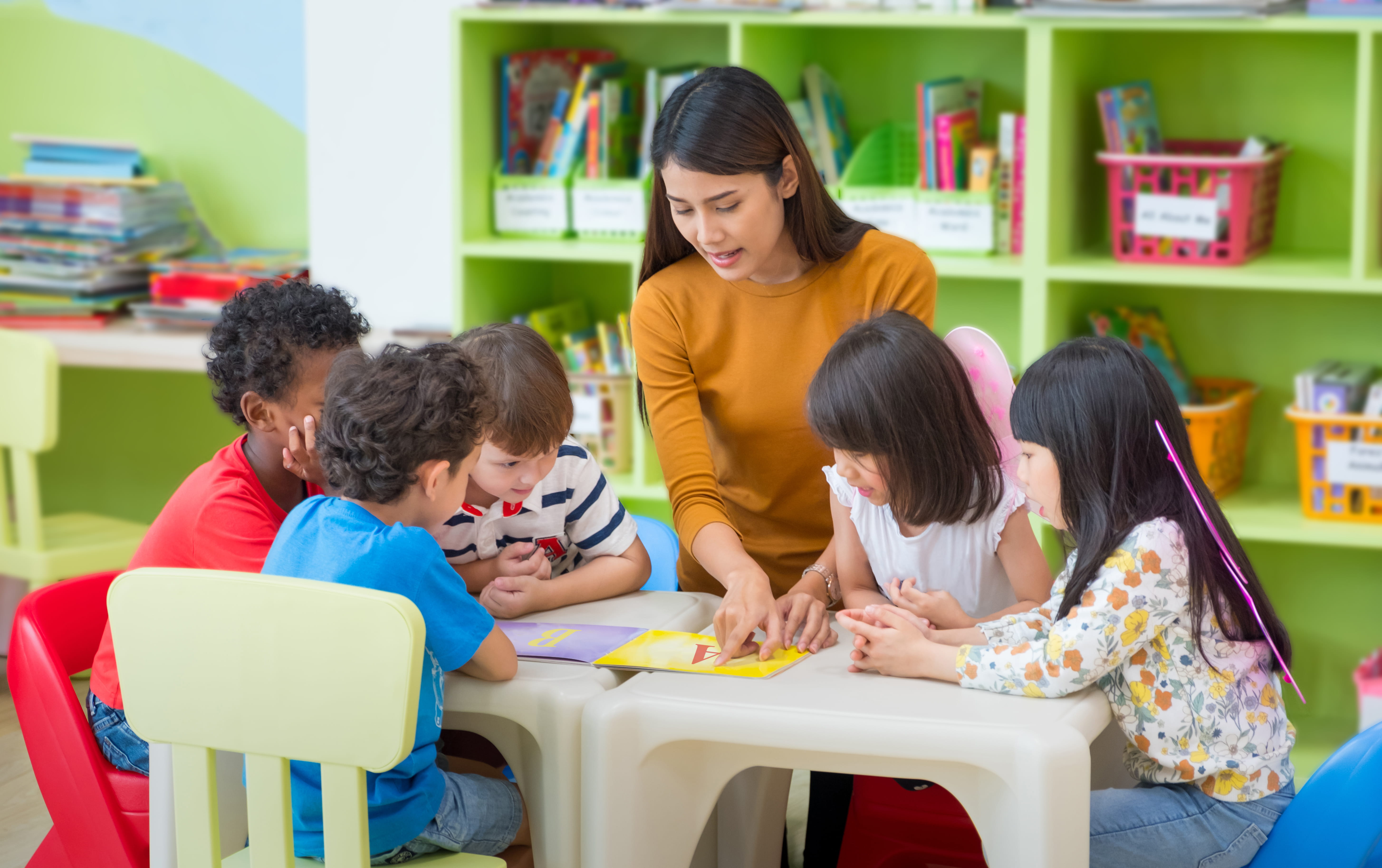 Female teacher teaching kids and reading a book with them in classroom