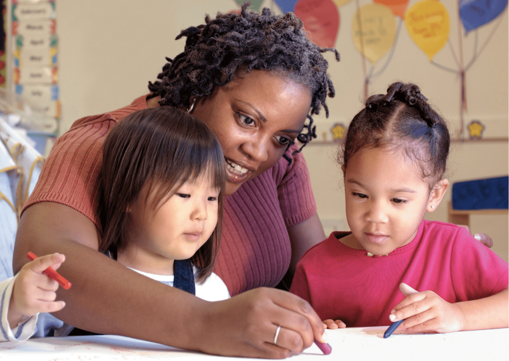 Lady drawing with two young kids in classroom, using crayon