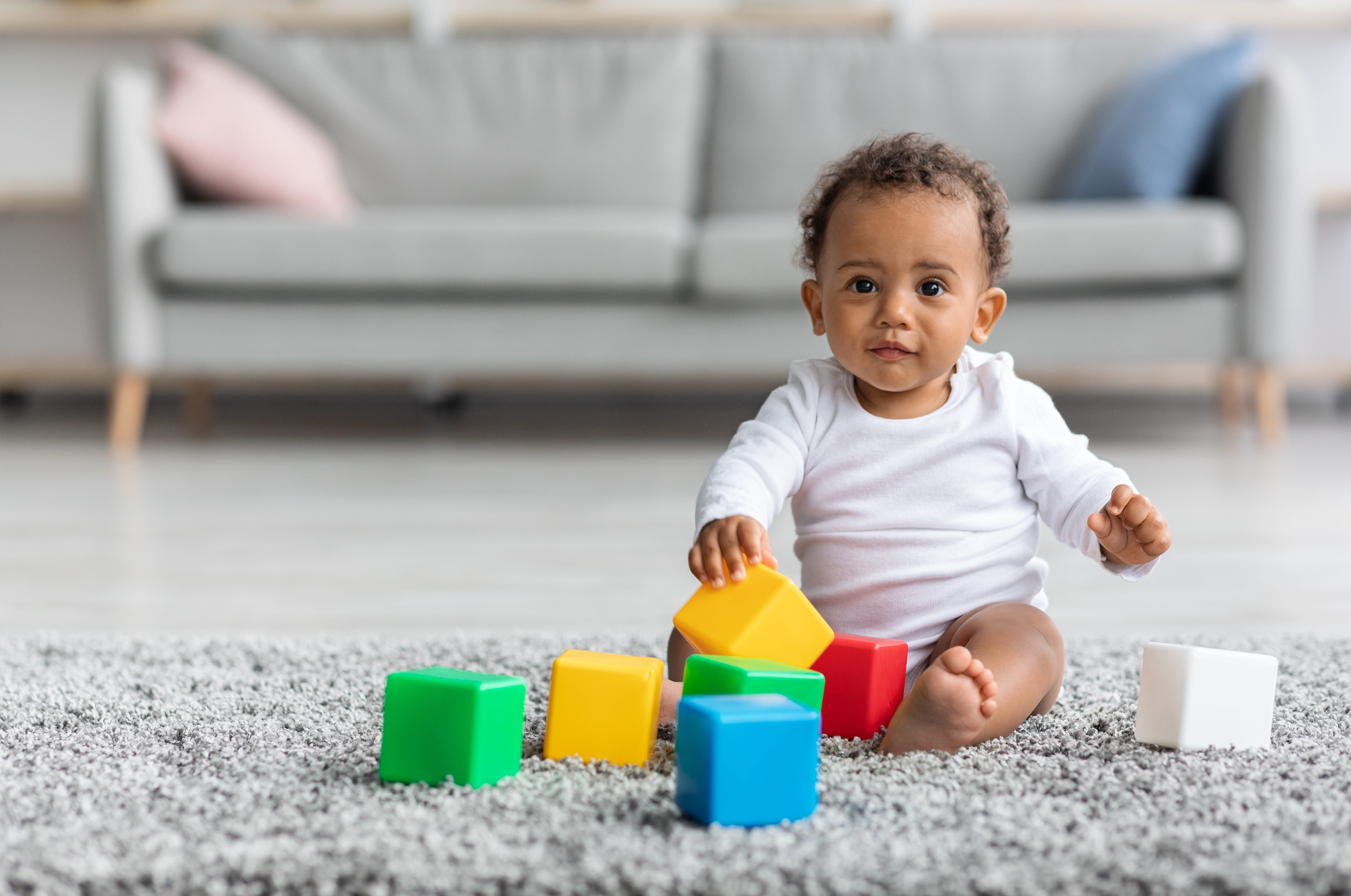 Infant Baby Playing With Stacking Colourful Building Blocks While Sitting On Carpet In House