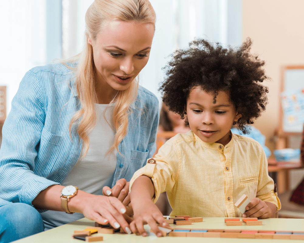 Teacher helping young child with wooden learning game in Montessori class.
