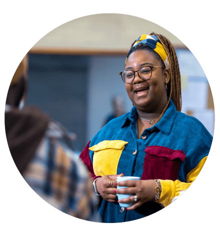 Community coffee morning, lady smiling and talking to fellow community member while holding a cup of coffee in her hand