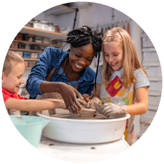 Two children and a lady smiling whilst doing pottery together